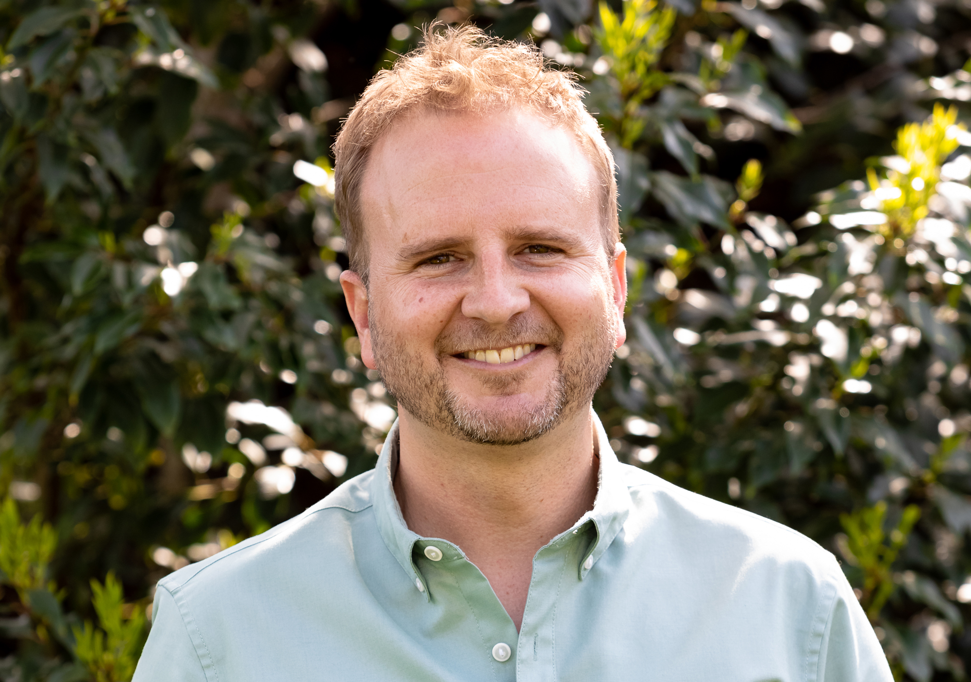 Portrait of Matthew Childs outdoors in front of green leaves