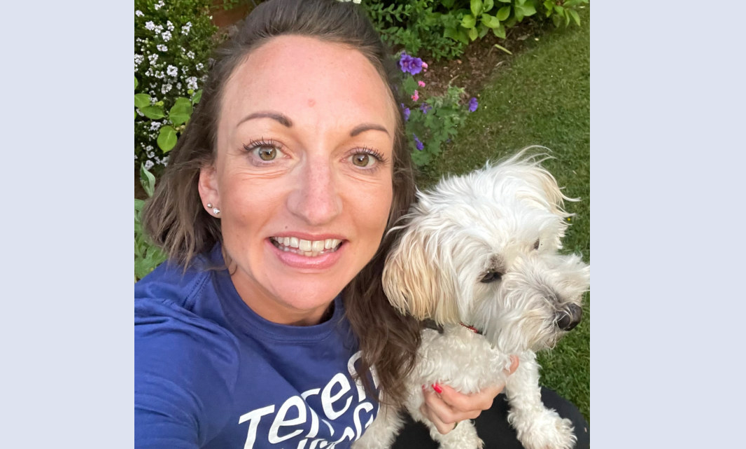 Sarah Ashford smiling at camera and holding a small white dog